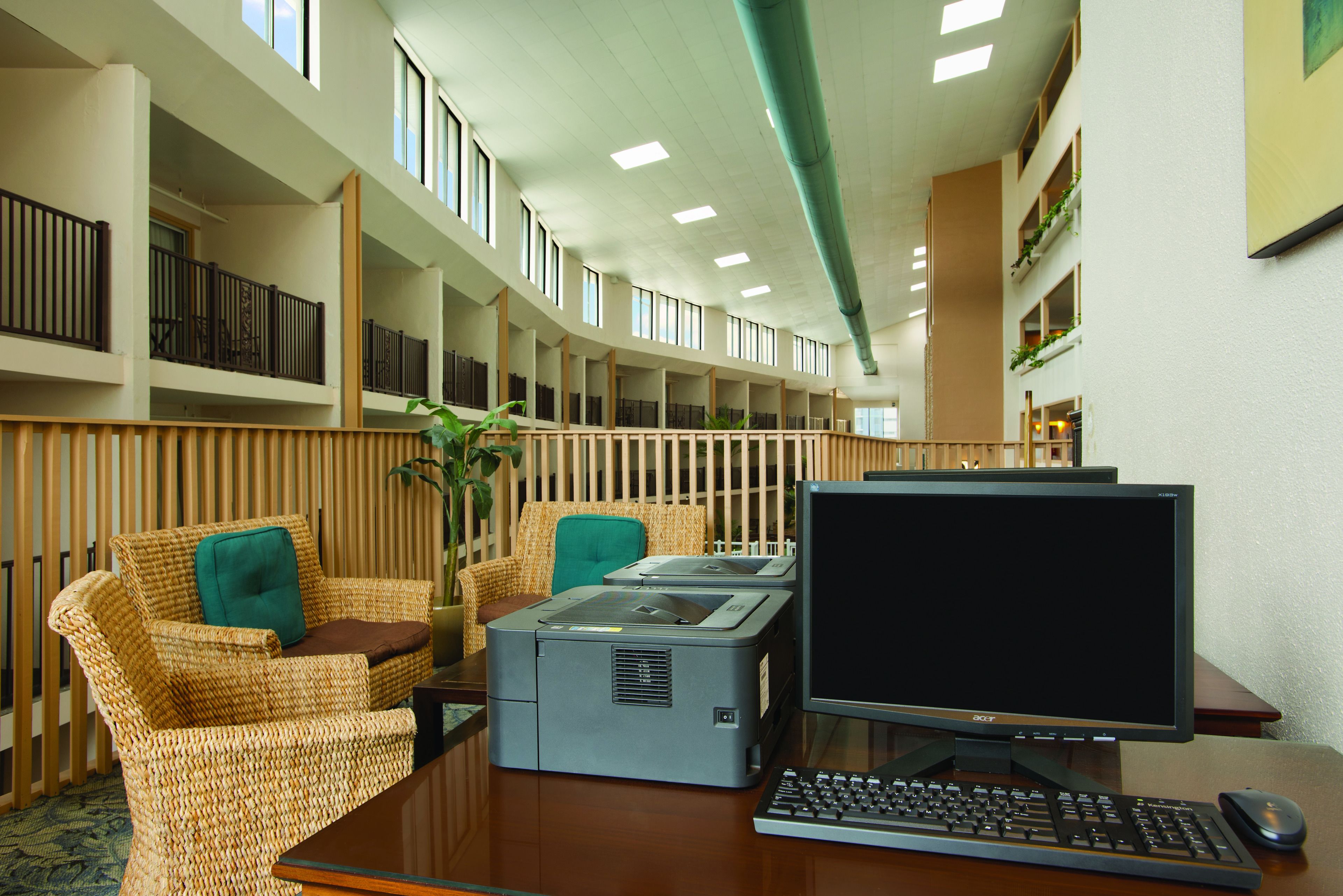 A hotel lobby with a long reception desk, wicker chairs, a large printer, and a computer monitor.
