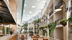 A spacious indoor dining area with multiple wooden tables and chairs, a long counter with a cash register, and hanging plants. - Quality Inn Oceanfront (Ocean City)