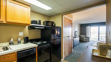 A compact kitchen with a stove, microwave, refrigerator, and dishwasher. There is a small seating area with a chair and a table.