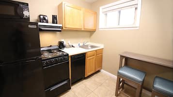 A compact kitchen with a refrigerator, stove, dishwasher, wooden cabinets, a sink, and two bar stools.
