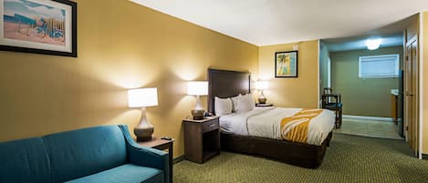 Hotellihuone, jossa on sänky, sohva, kaksi yöpöytää valaisimineen, seinällä oleva kehystetty taulu ja matolla peitetty lattia.