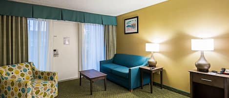 Une chambre d’hôtel avec un fauteuil à motifs, un canapé bleu, une petite table, deux lampes de chevet et un tableau encadré au mur.
