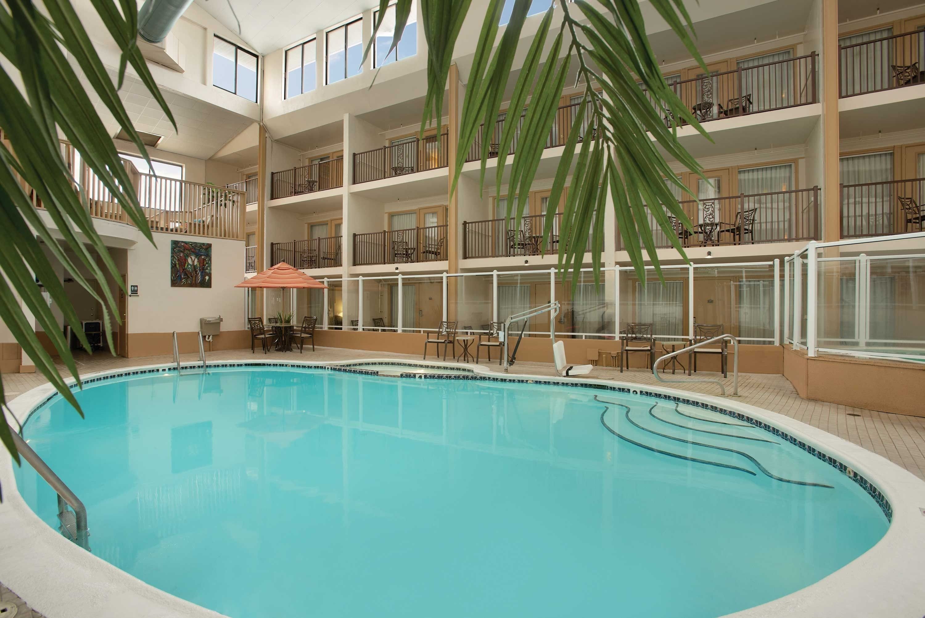 A large indoor swimming pool with multiple balconies, surrounded by indoor seating areas and a tropical plant.