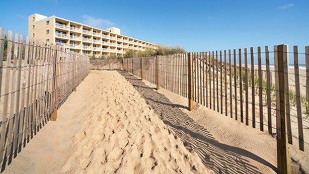 A sandy pathway leading to a building with multiple balconies, surrounded by a wooden fence. - Quality Inn Oceanfront (Ocean City)