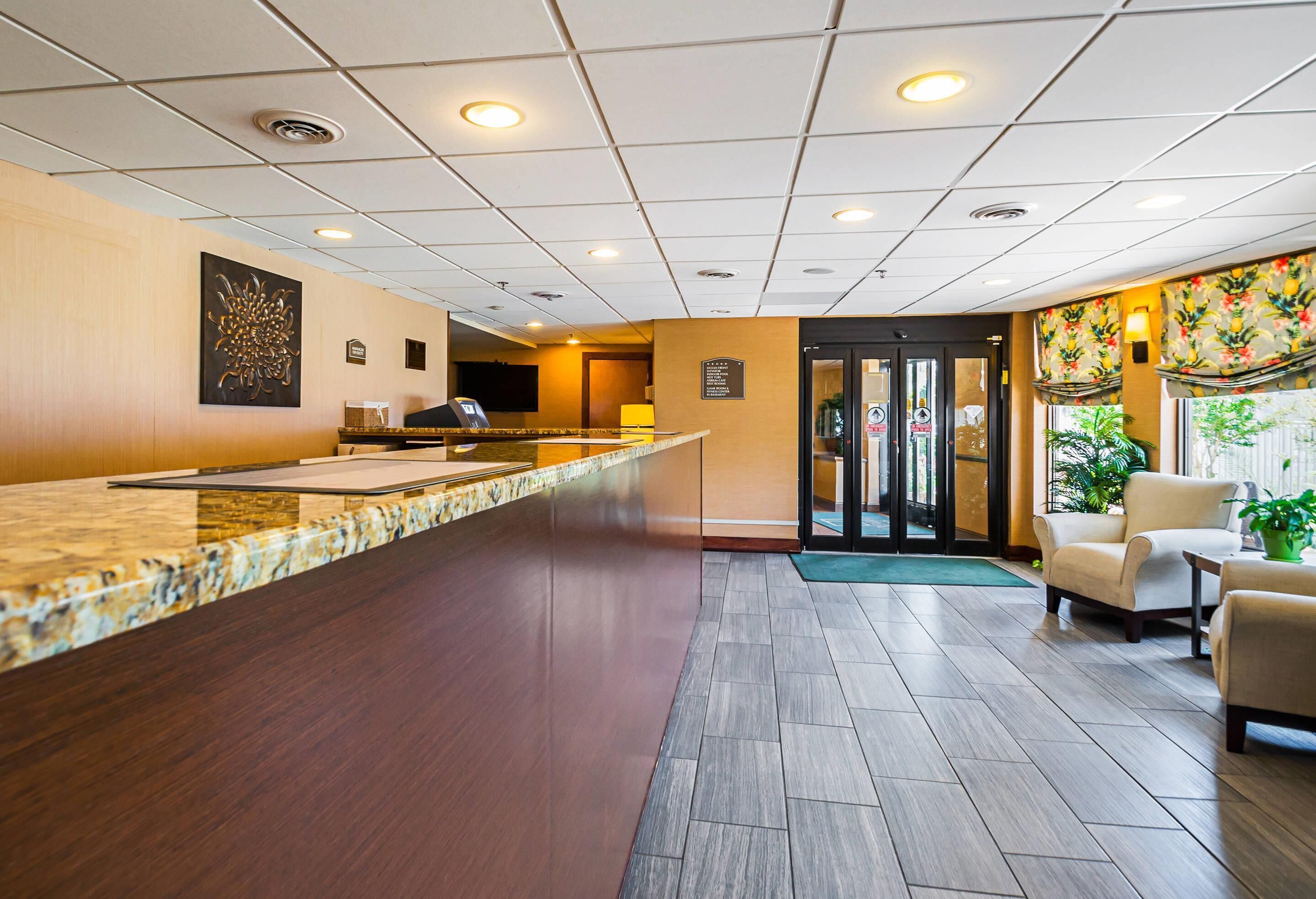 Een hotel lobby met een receptiebalie, een kiosk voor digitaal inchecken, een zithoek met stoelen en een deur naar de kamers.