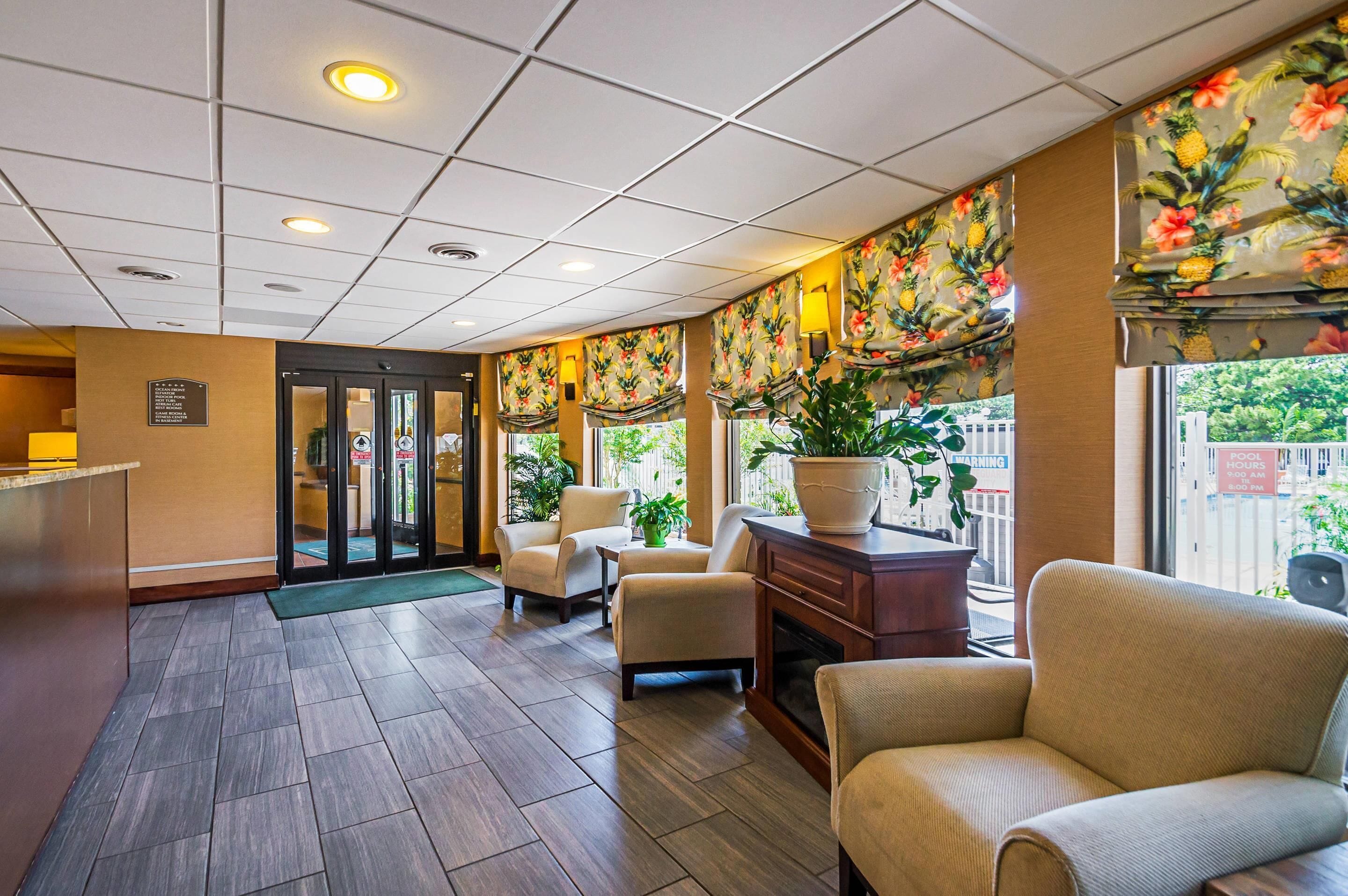 Un hall d’hôtel comprenant un comptoir d’accueil, un espace salon et de grandes fenêtres décorées dans un style tropical.