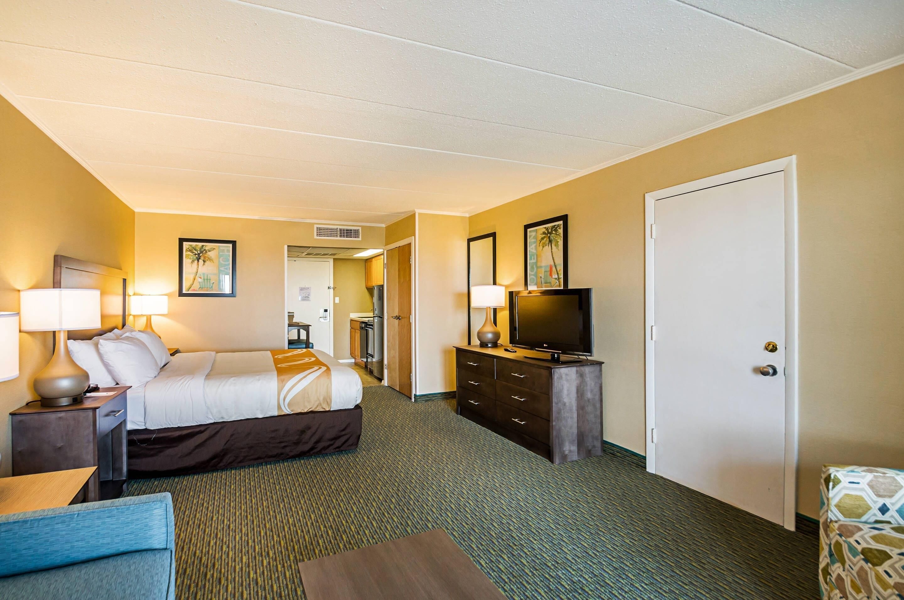 Ein Hotelzimmer mit Bett, Fernseher, Schreibtisch und Stuhl. Eine Tür und ein Fenster sind vorhanden.