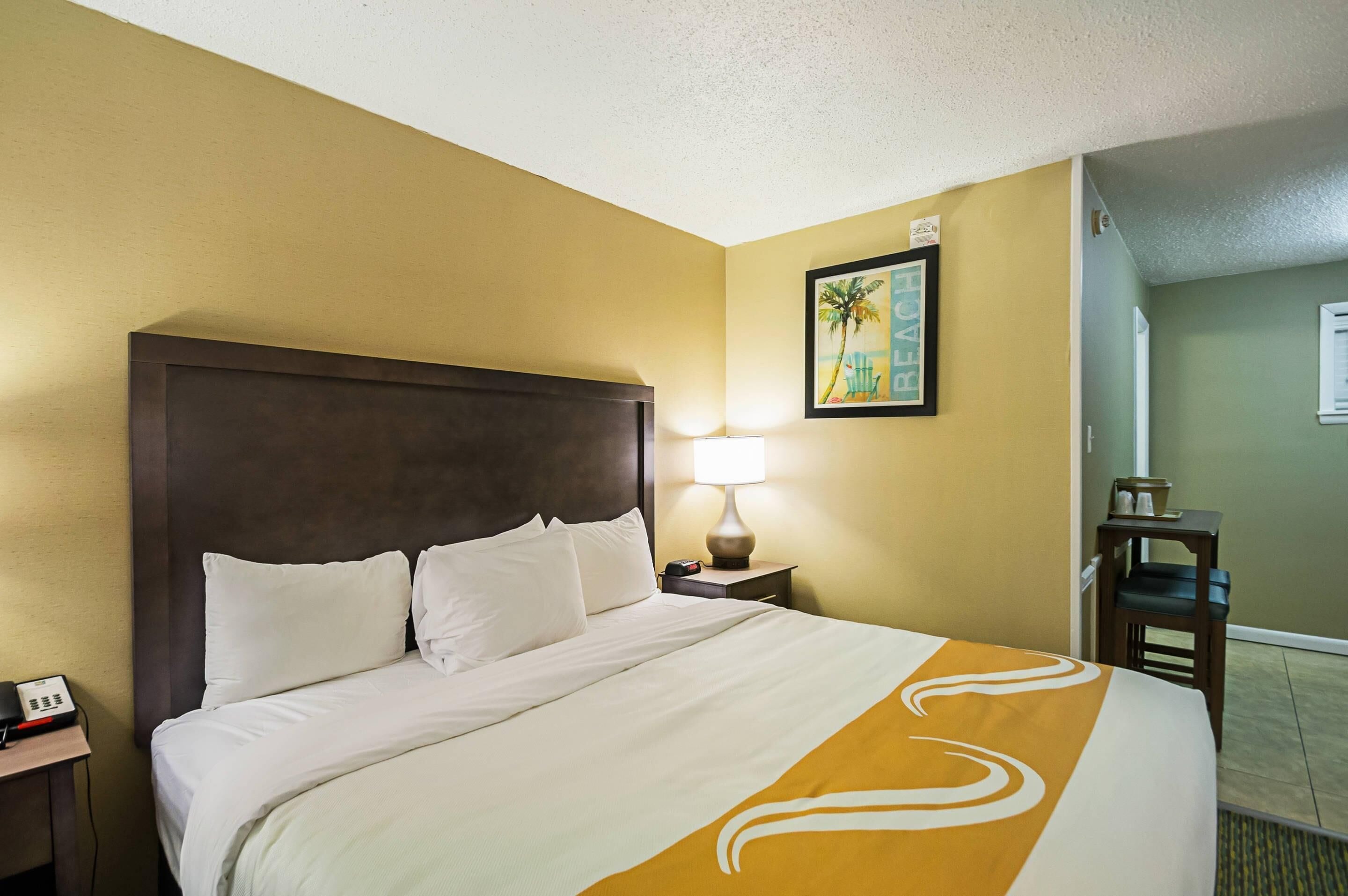 Een hotelkamer met een groot bed, een nachtkastje met een lamp, een klein tafeltje met een telefoon en een stoel.