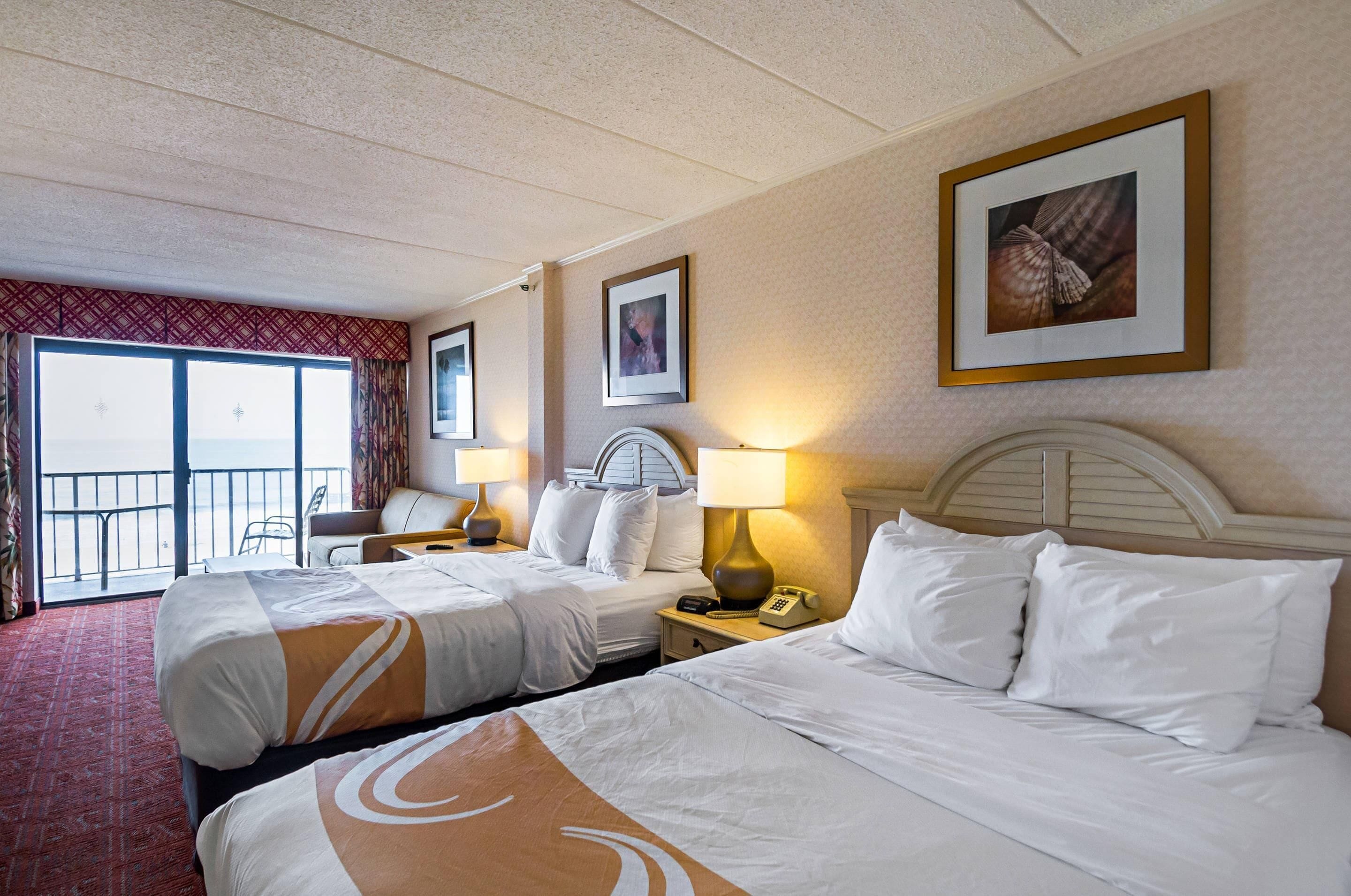 A hotel room with two beds, a balcony, and a view of the sea.