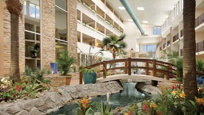 A hotel atrium with a central water feature, a wooden bridge, and multiple balconies with plants. - Quality Inn Oceanfront (Ocean City)