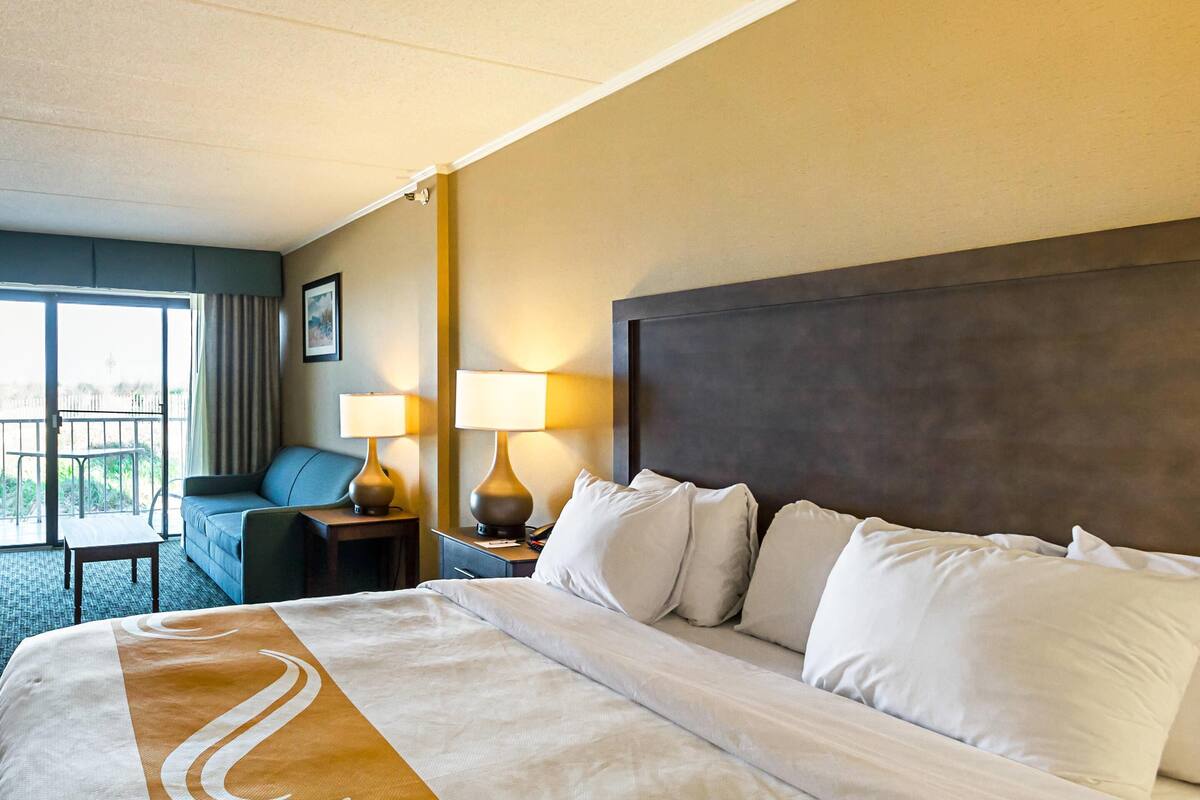 Camera d'albergo con un letto grande, un divano, due lampade da comodino, un comodino e vista all'esterno tramite una porta scorrevole.