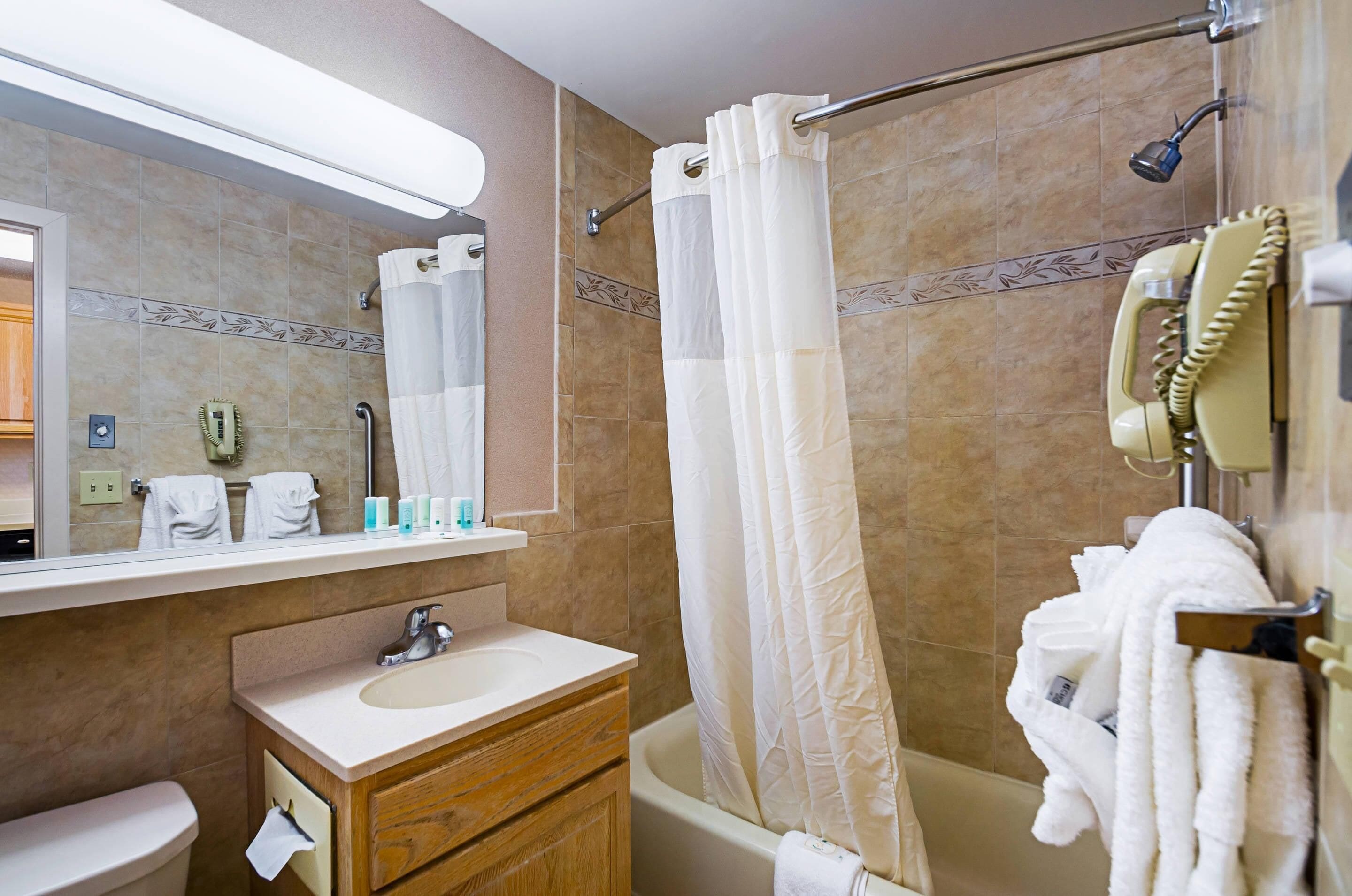 A bathroom with a bathtub, a shower curtain, a vanity with a sink, and a mirror.