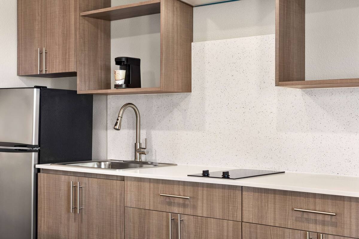A modern kitchen with wooden cabinets, a stainless steel refrigerator, a sink, and a coffee maker on the countertop.