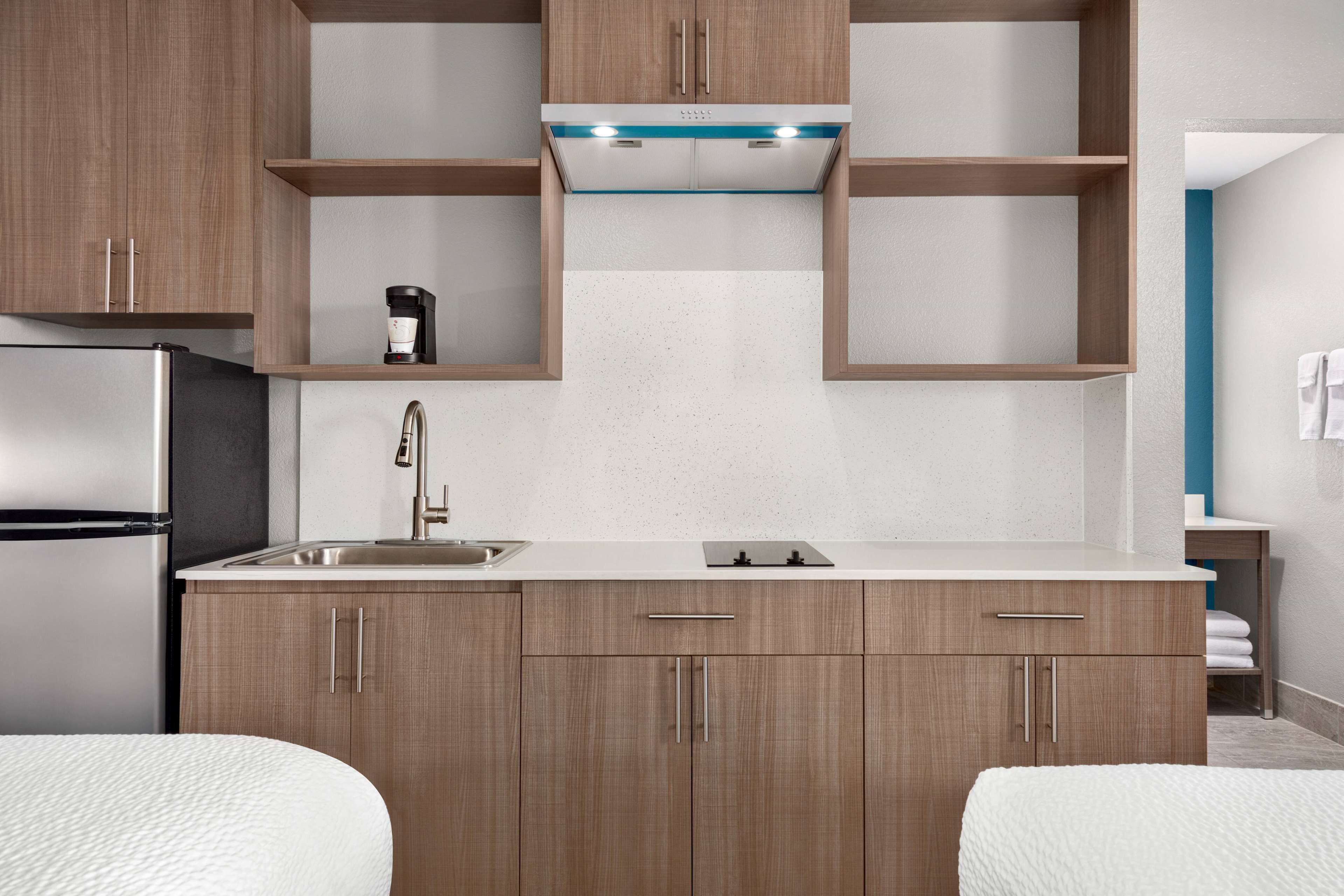 Una cocina moderna con armarios de madera, un refrigerador de acero inoxidable, un lavamanos y una cafetera.