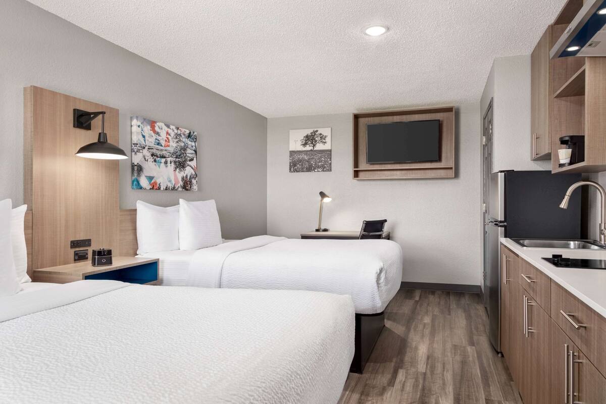 A hotel room with two beds, a kitchenette, and artwork on the walls.