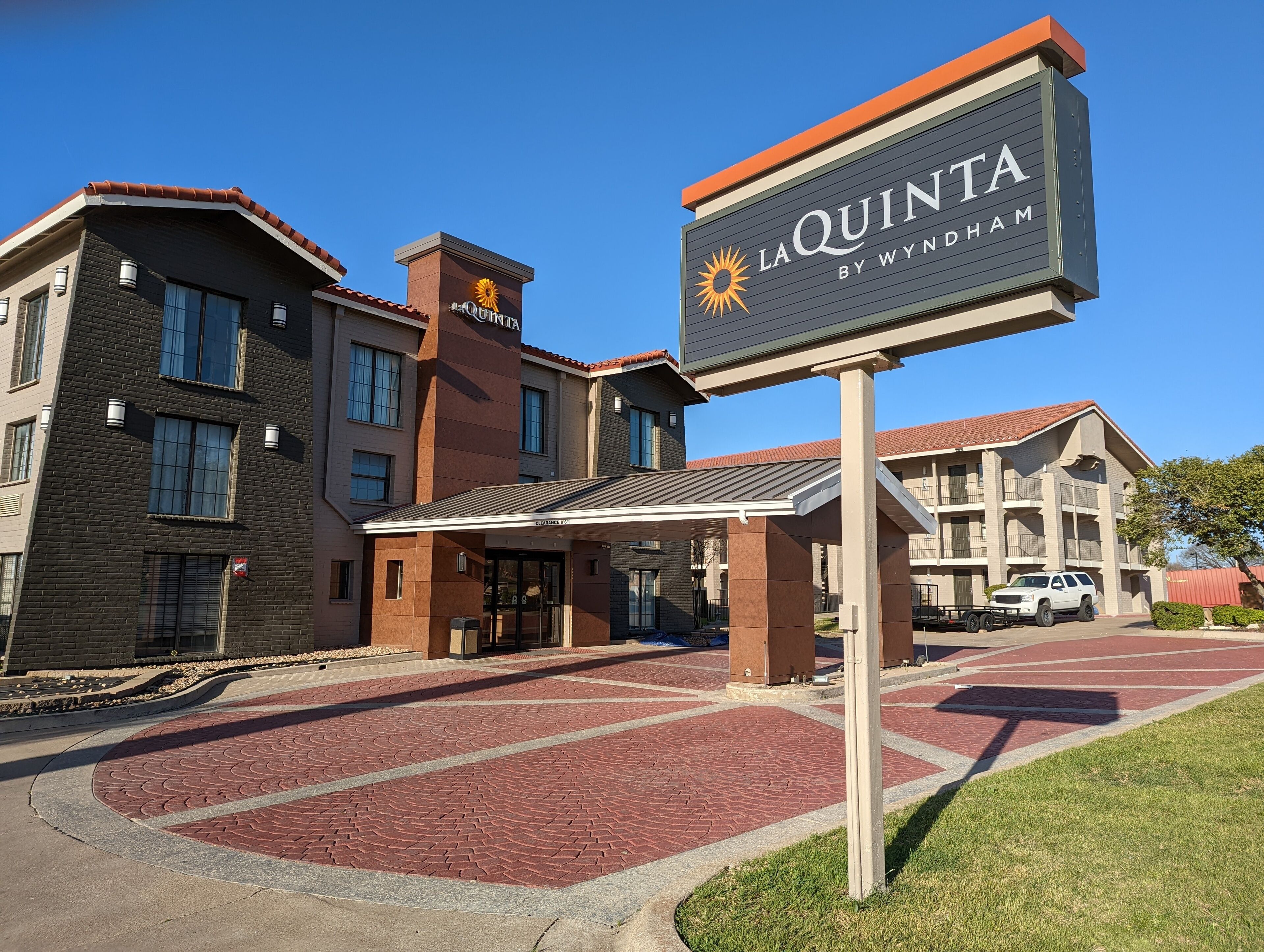 Un hotel llamado La Quinta by Wyndham con una entrada despejada, un área de estacionamiento y un camino de ladrillo que conduce a la entrada.