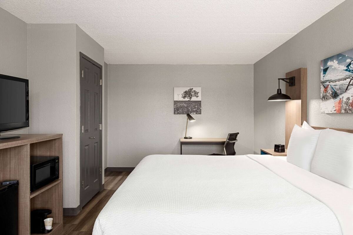 A hotel room with a bed, a desk, a chair, a television, and a painting on the wall.
