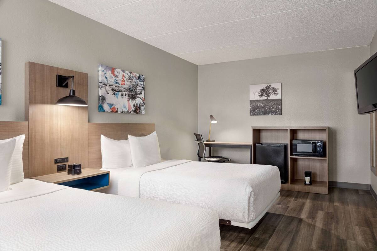 A hotel room with two beds, a desk with a computer, a TV, and artwork on the walls.