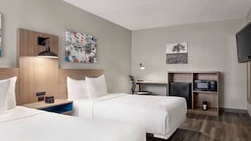 A hotel room with two beds, a desk with a computer, a TV, and artwork on the walls.
