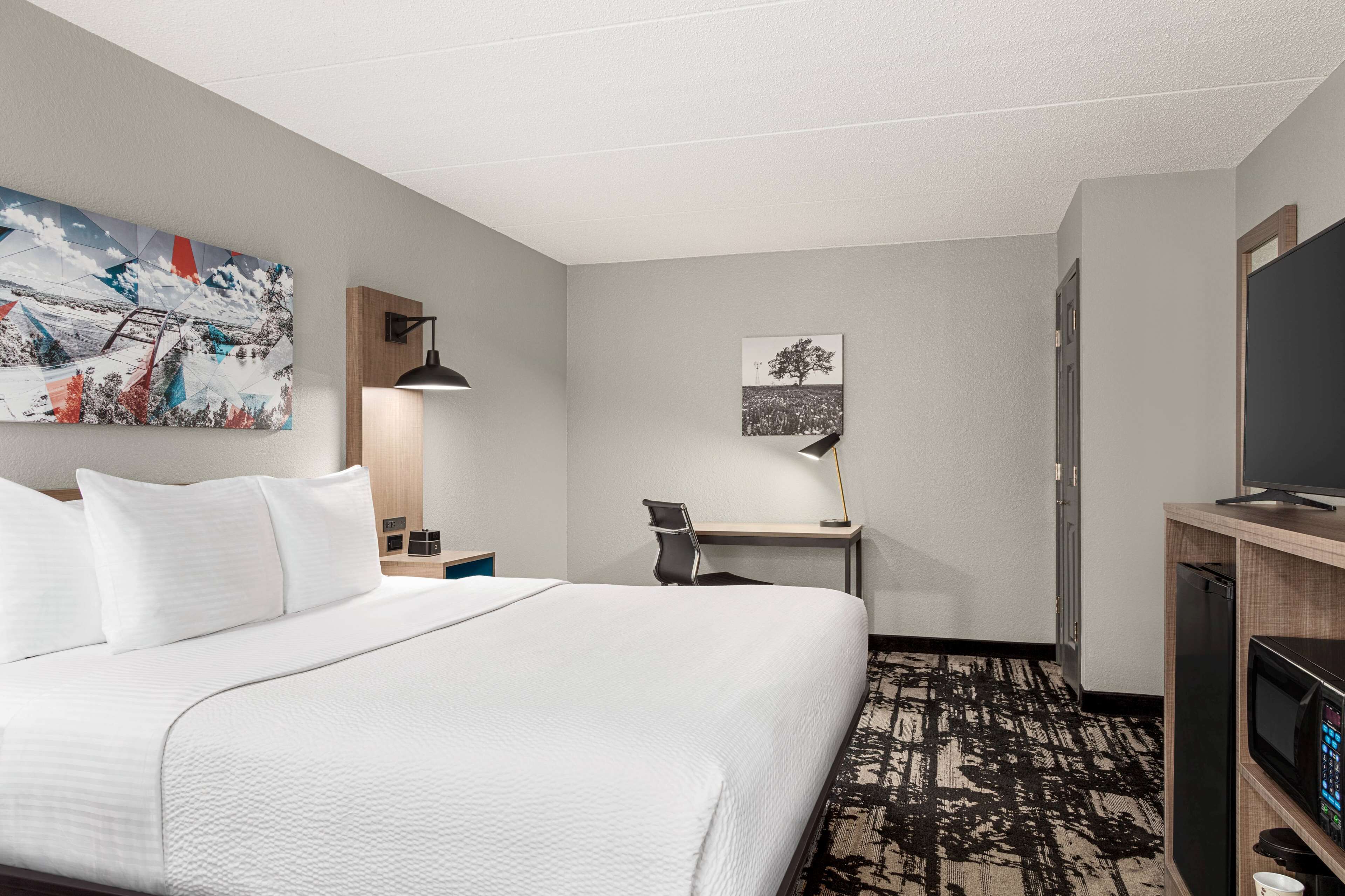 Une chambre d’hôtel avec un grand lit, un bureau avec une chaise, une télévision et des œuvres d’art accrochées aux murs.