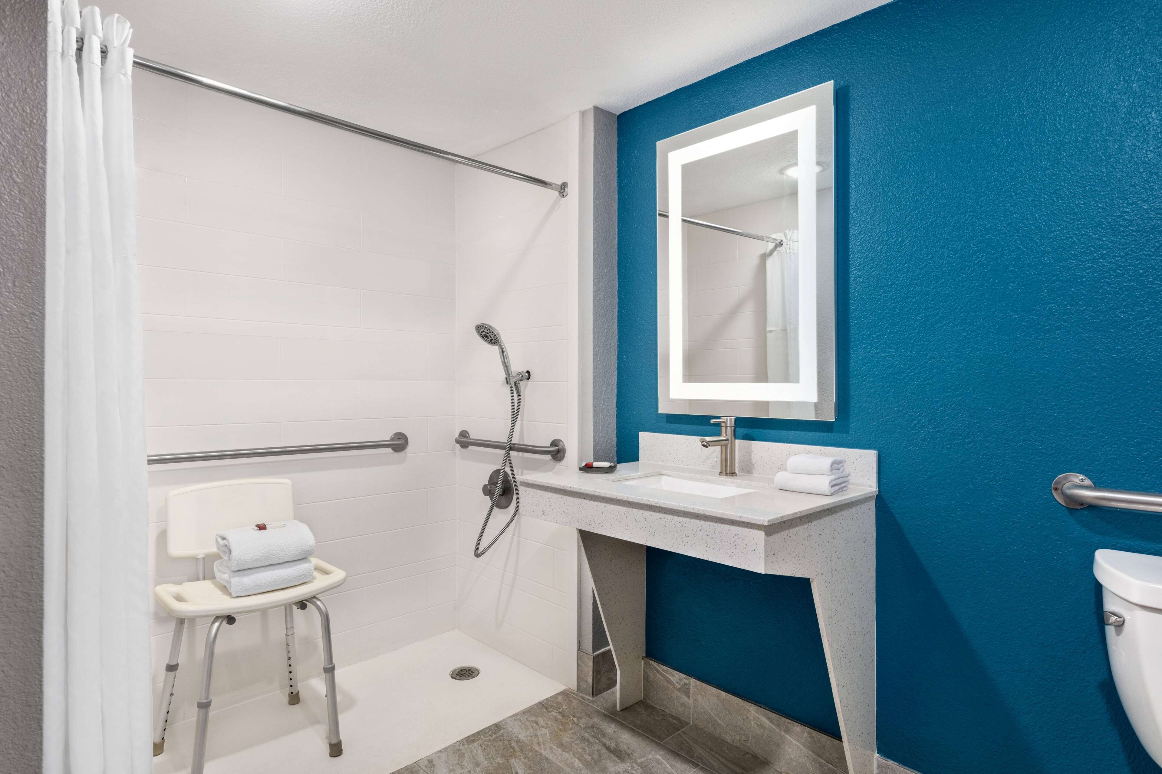 A modern bathroom with a shower, a white sink, and a blue accent wall.
