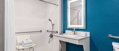 A modern bathroom with a shower, a white sink, and a blue accent wall.