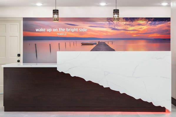 A reception desk with a large mural of a sunset over water, a wooden counter, and two pendant lights. - La Quinta Inn by Wyndham Temple (Temple)
