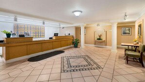 A hotel lobby with a reception desk, a tiled floor, a seating area, and a decorative rug.