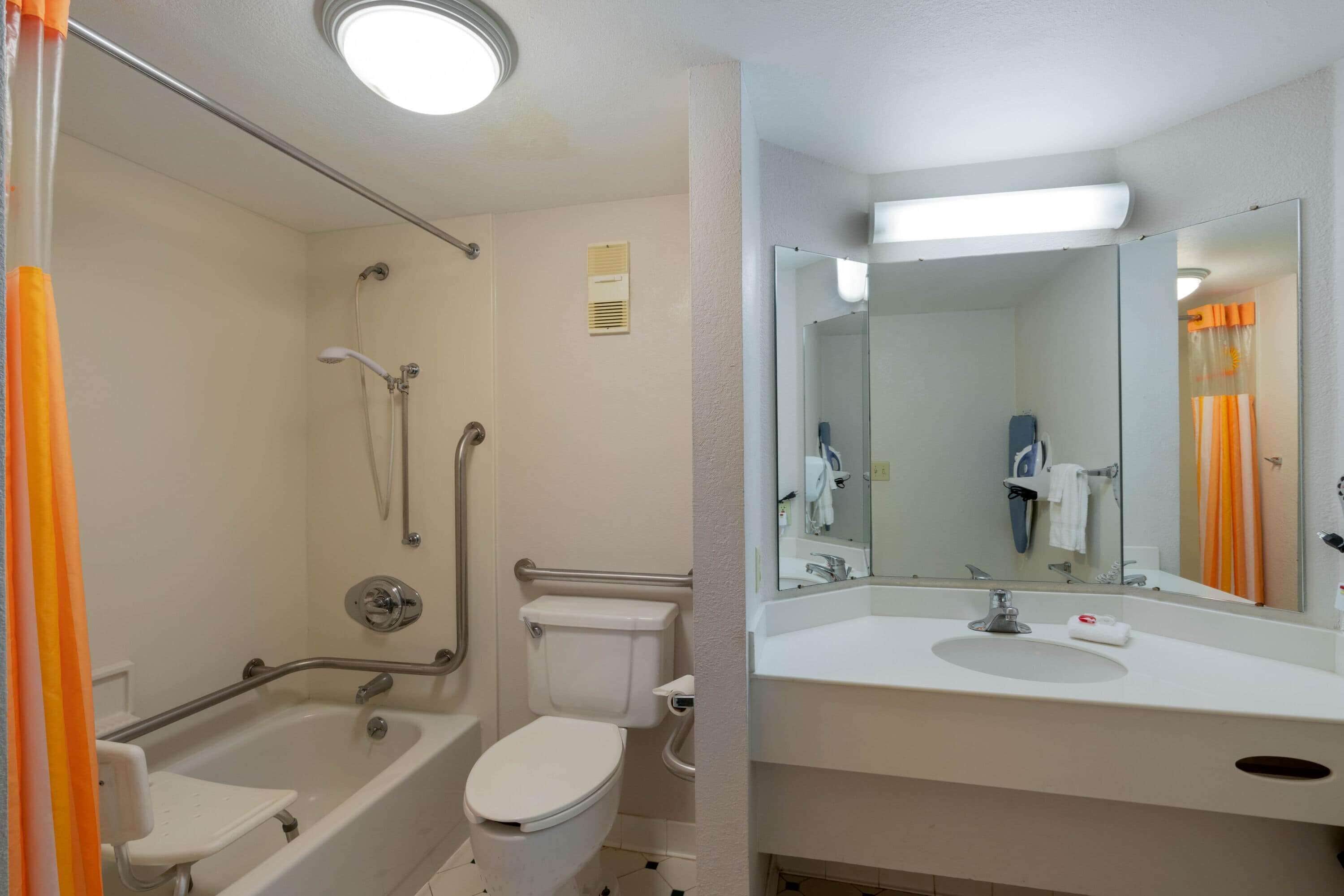 A bathroom with a bathtub, toilet, and sink, equipped with a handrail and a mirror.