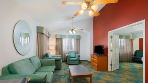 A hotel room with a green sofa, a wooden coffee table, a TV, and a ceiling fan.
