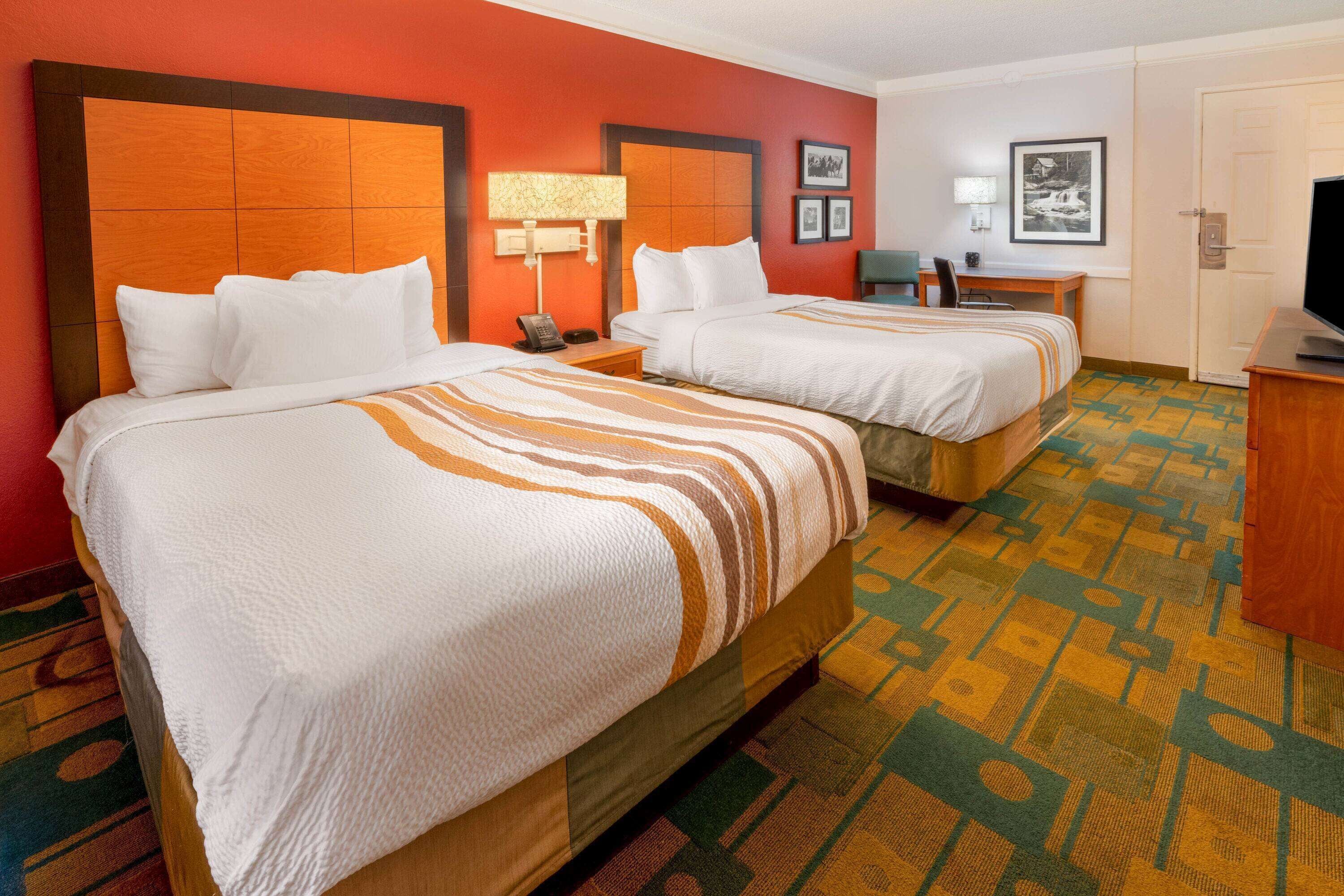 A hotel room with two beds, a desk, a chair, a television, and a patterned carpet.