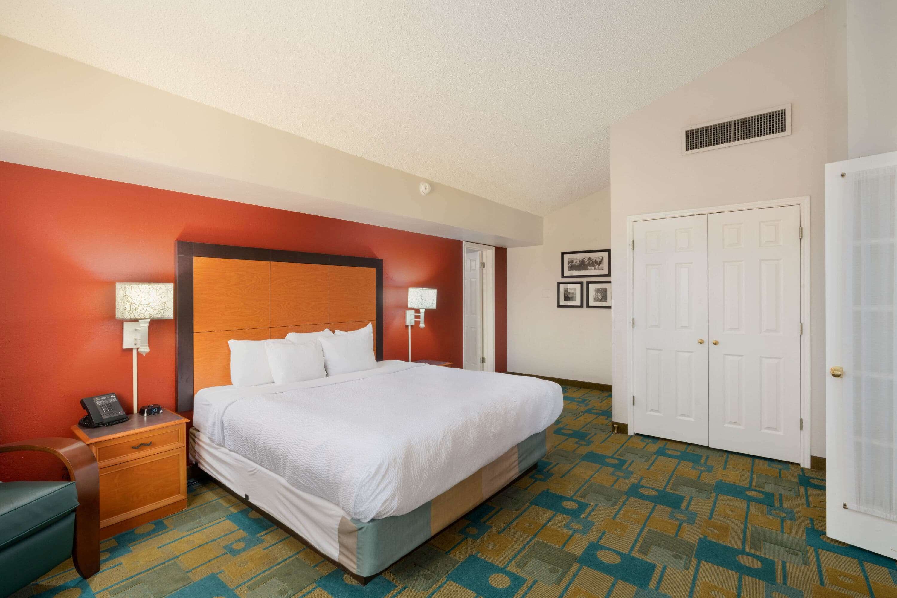 A hotel room with a bed, nightstand, lamp, and a door.
