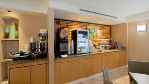 A hotel breakfast area with a coffee machine, refrigerator, and a counter with various items.