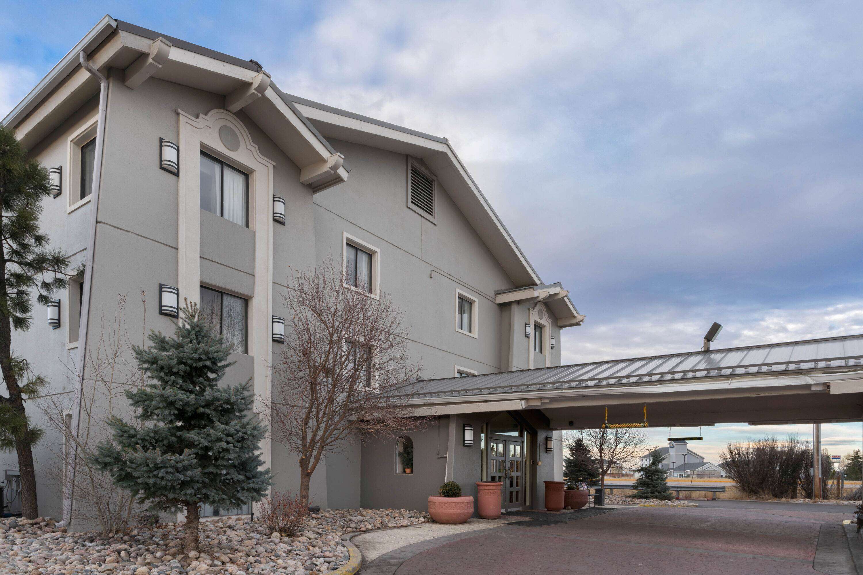 A modern building with a covered entrance, large windows, and a landscaped area with trees and rocks.