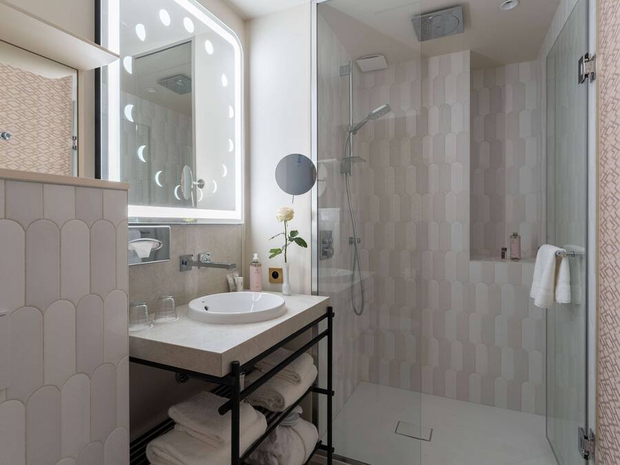 Un baño moderno con ducha envuelta en vidrio, tocador con lavamanos y un espejo grande.