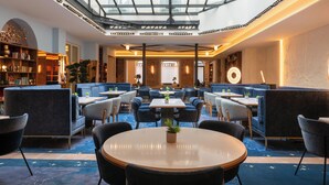 A modern hotel lobby with a glass ceiling, seating areas, and a central table with a plant. - Hôtel Astra Opéra - Astotel (Paris)