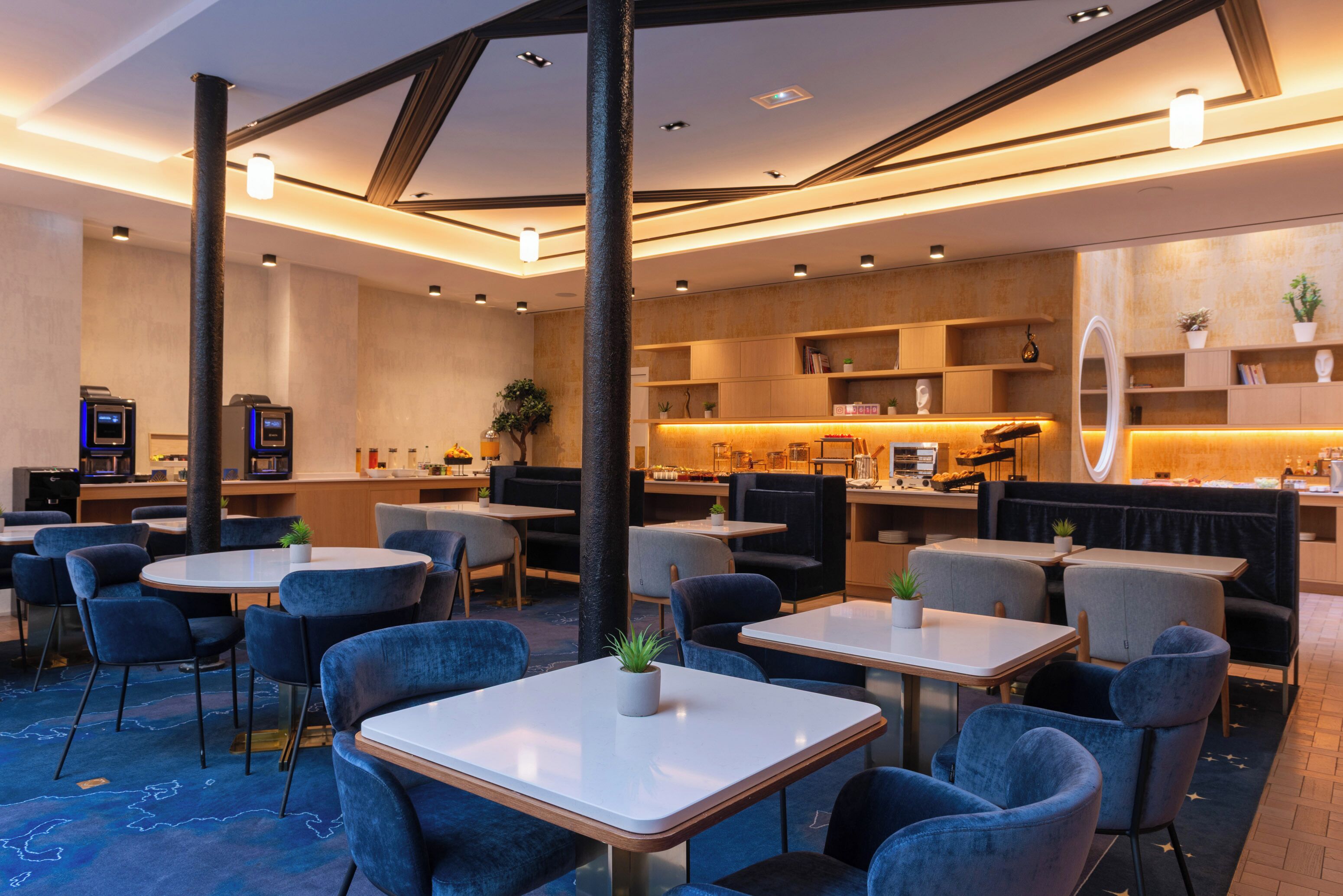 Un ristorante moderno con tavoli rotondi, sedie blu e un'area bar centrale.