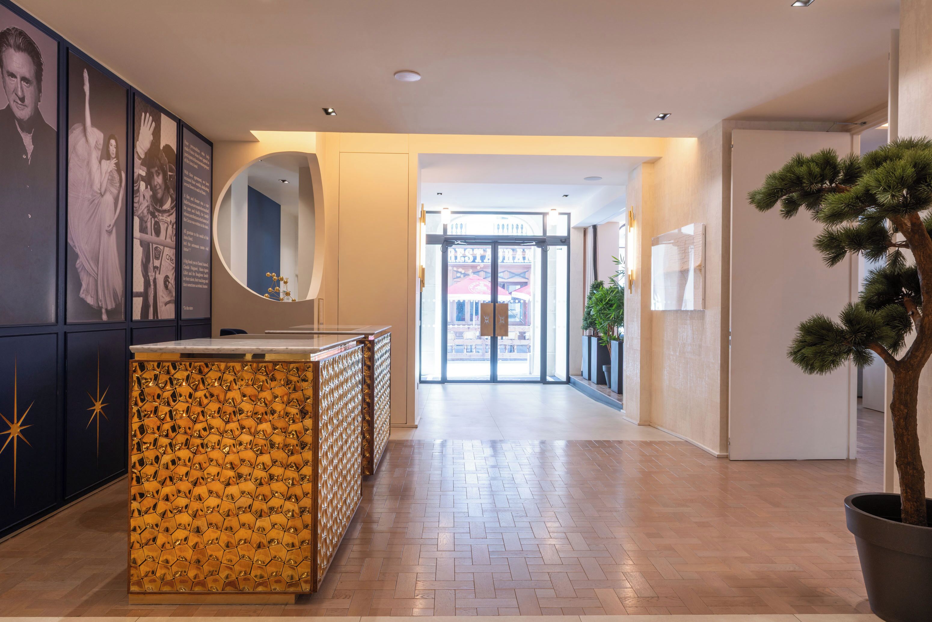 Eine Hotelhalle mit einer Rezeption, einem großen Spiegel, einem Blumentopf und einer Tür zum Restaurant.