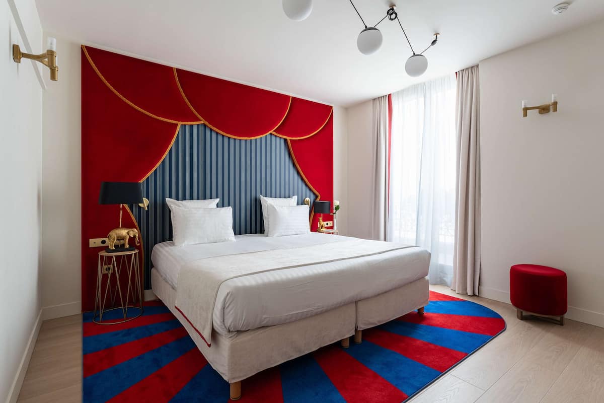 Una habitación de hotel moderna con una cama grande, un tapete azul y rojo a rayas y una pared de acento roja.