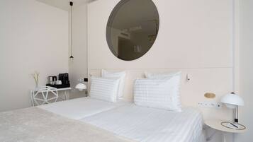 Une chambre moderne avec un grand lit, un miroir rond, une table de chevet avec une lampe et une petite table blanche sur laquelle se trouve une machine à café.