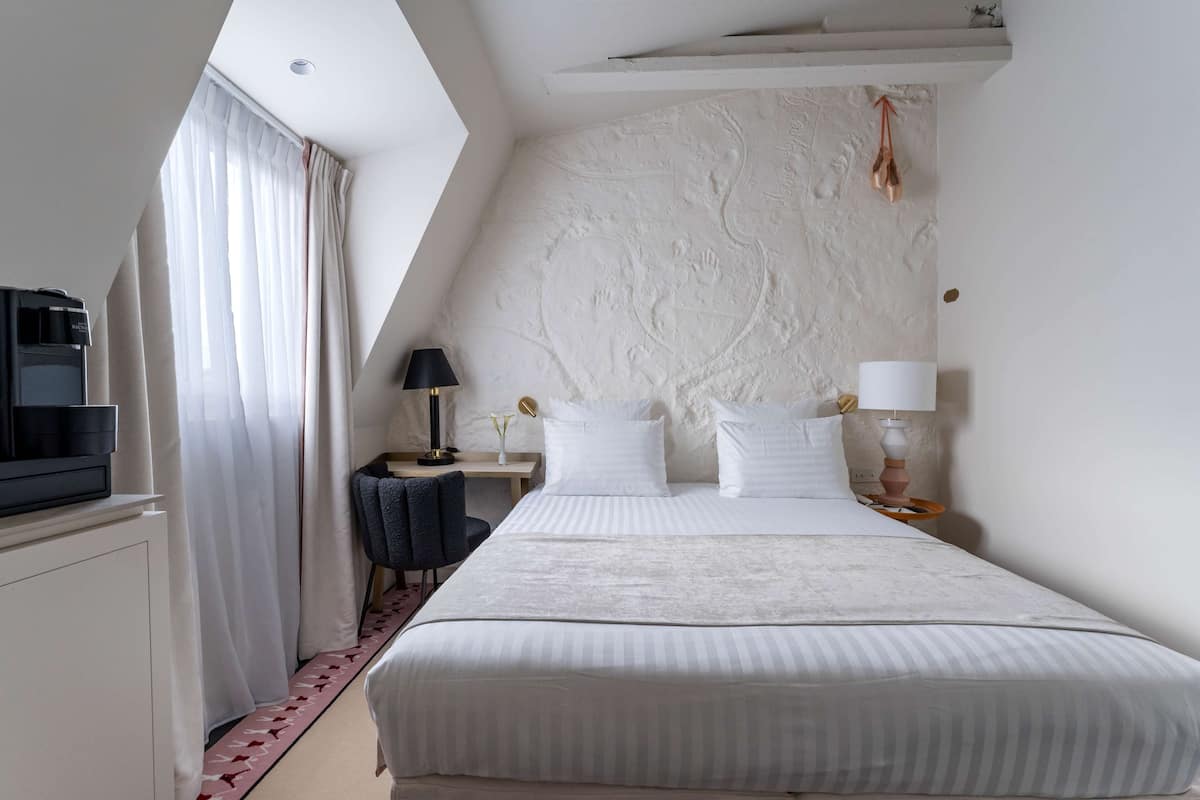 Habitación de hotel con una cama grande, un escritorio con lámpara, una silla y un televisor sobre un mueble.