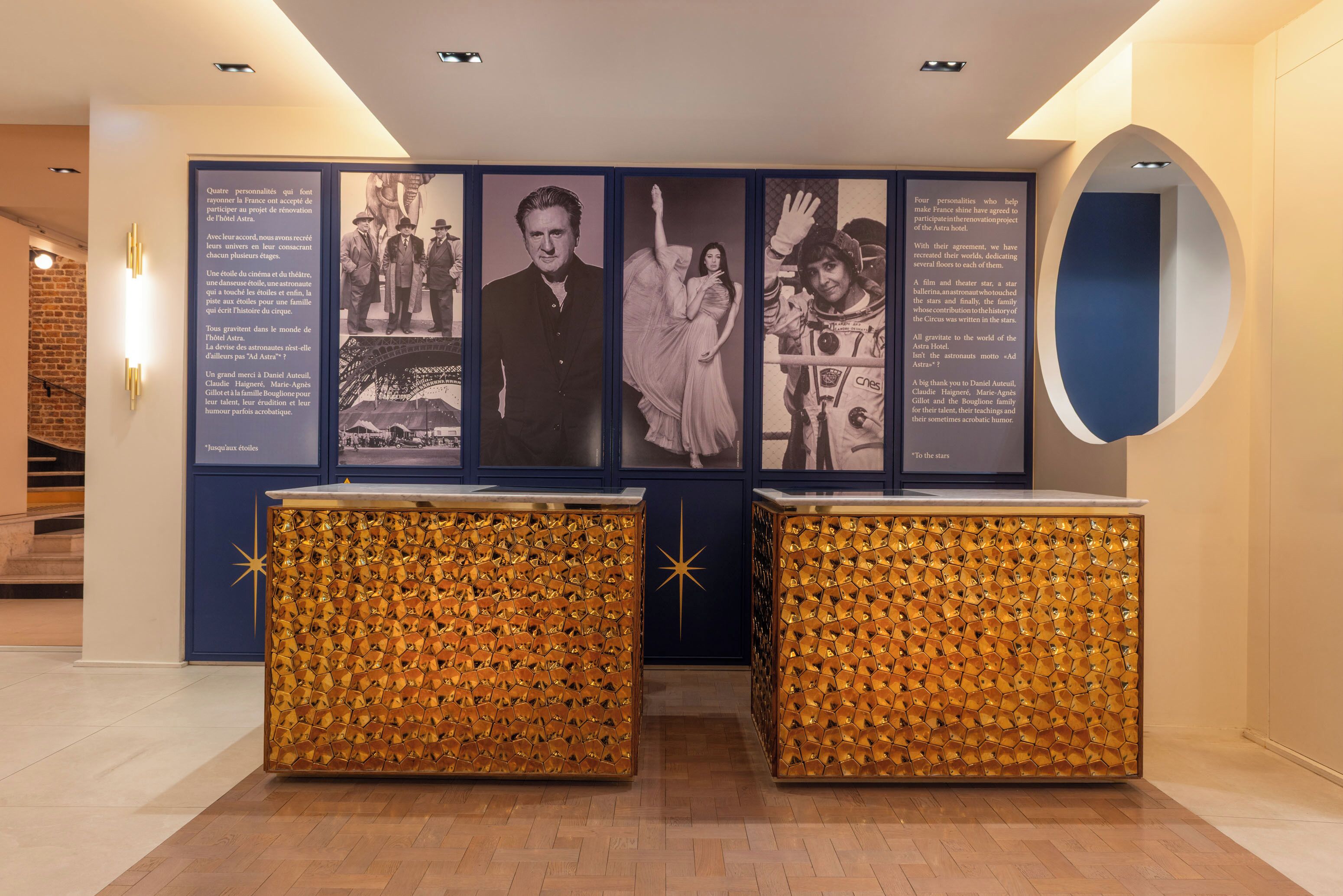 A reception area with a wall displaying historical photos and text, two decorative gold-patterned stands, and a round mirror.