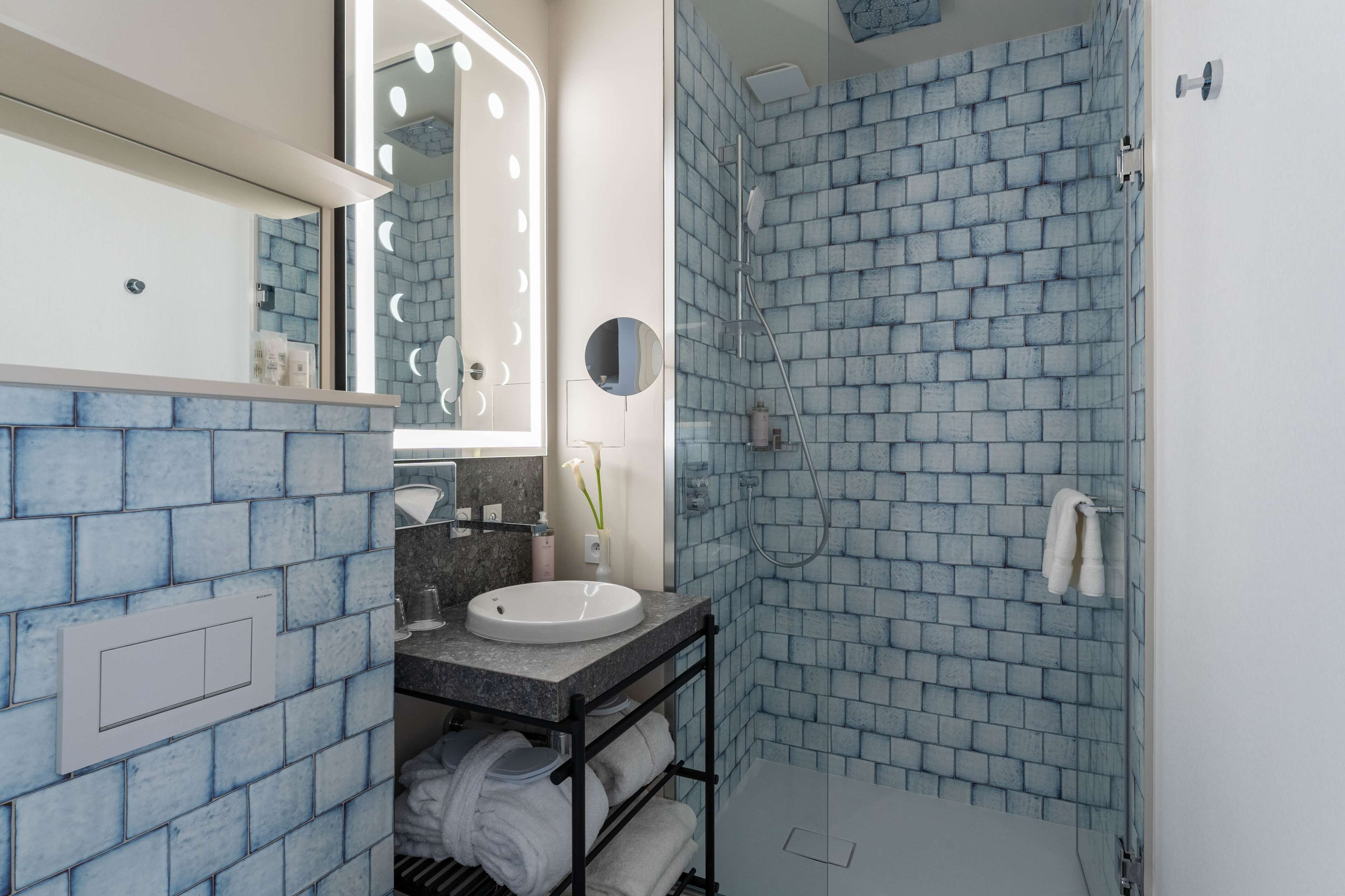 Een badkamer met een blauwe bakstenen muur, een witte wastafel, een spiegel met verlichting en een douchehoek.
