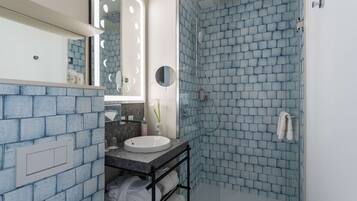 Een badkamer met een blauwe bakstenen muur, een witte wastafel, een spiegel met verlichting en een douchehoek.