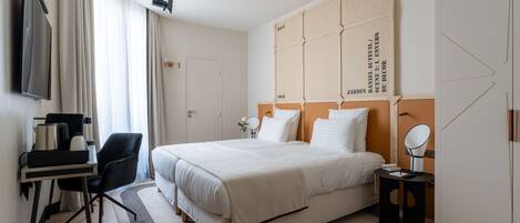 A modern hotel room with a large bed, a desk with a chair, a TV, and a wardrobe.