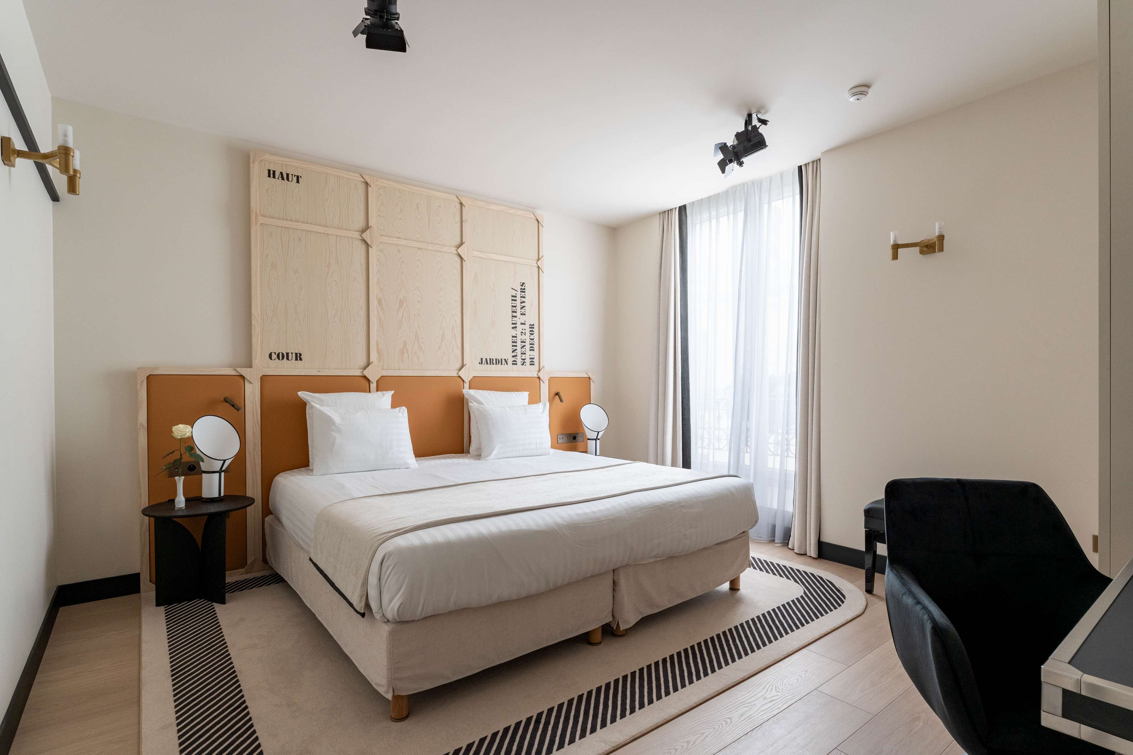 Una habitación de hotel con una cama grande, dos mesitas de noche, una silla negra y una ventana con cortinas.