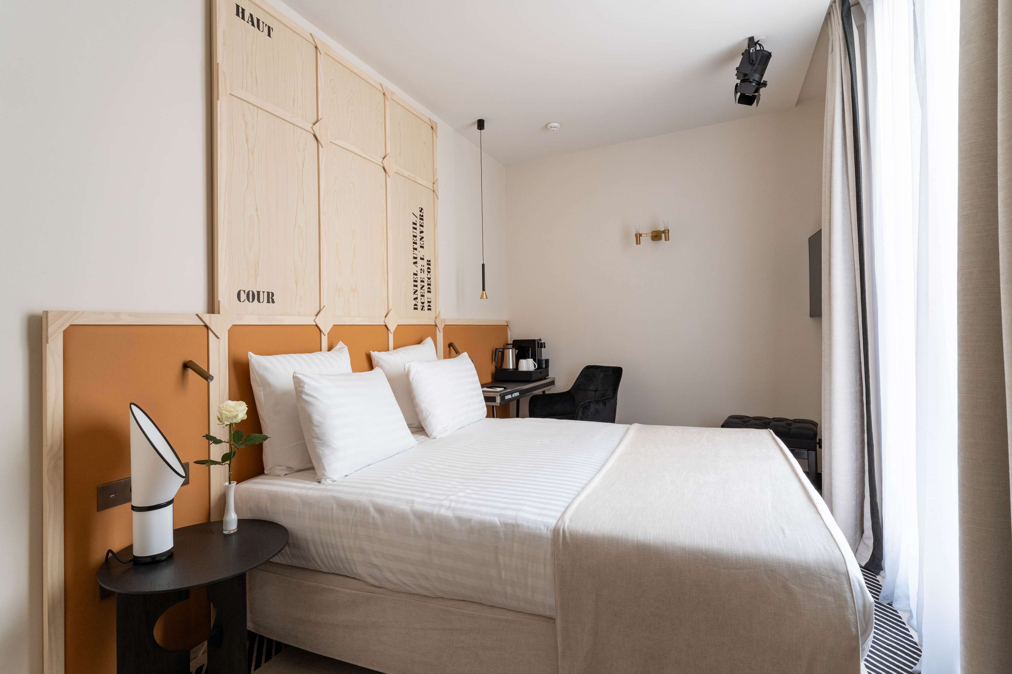 A hotel room with a bed, bedside table, and a desk with a chair.