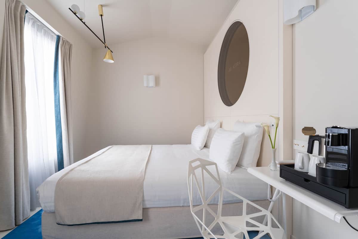 Una habitación de hotel con cama, escritorio con cafetera y ventana con cortinas.