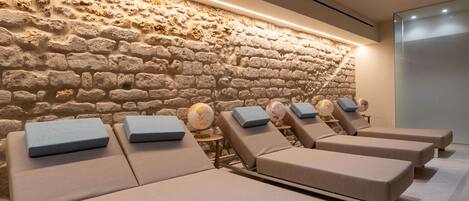 A spa area with stone walls, multiple sun loungers with cushions, and a globe decoration on one of the loungers.