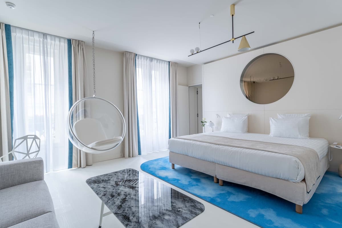 Un dormitorio moderno con una cama grande, una silla colgante y un espejo redondo en la pared.